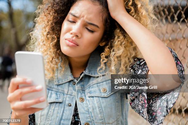 unhappy mixed race woman texting on cell phone - dificuldades em relações imagens e fotografias de stock