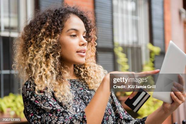 mixed race woman online shopping with digital tablet in city - crédit consommation photos et images de collection