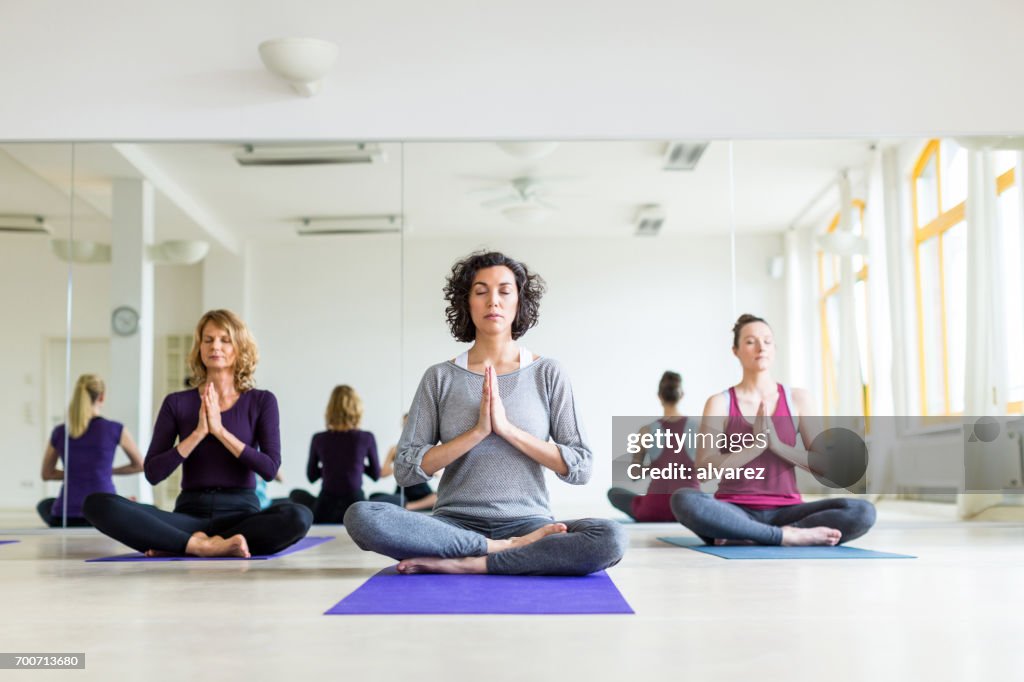 Grupo sano de hembras meditando en pose de yoga en la gimnasio