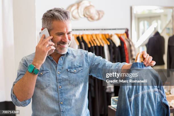 caucasian man examining shirt talking on cell phone - denim shirt stock pictures, royalty-free photos & images