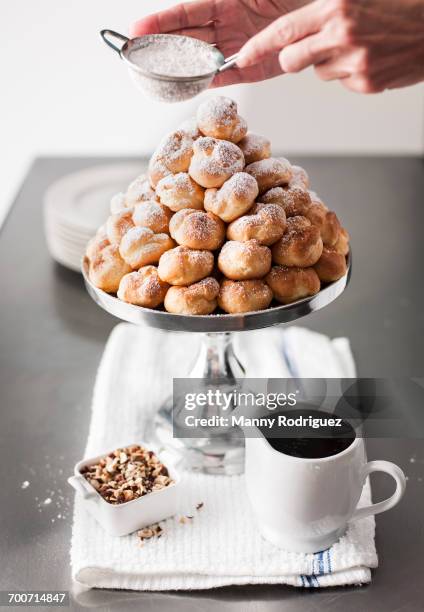 hands shaking powdered sugar onto tray of cream puffs - profiterole stock pictures, royalty-free photos & images