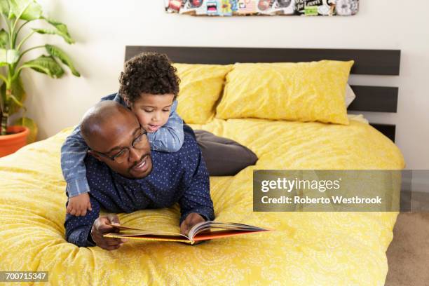 father reading book to son on bed - kids reading glasses stock pictures, royalty-free photos & images