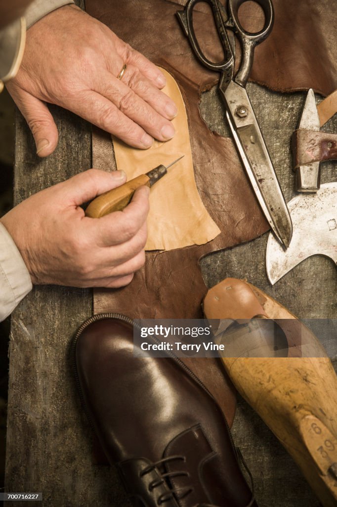 Hands of shoemaker using awl on leather