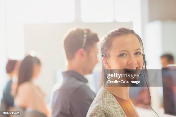 portrait smiling female telemarketer wearing headset in office - boss over shoulder stock pictures, royalty-free photos & images