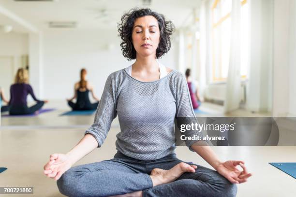 mature woman meditating in gym class - lotus position stock pictures, royalty-free photos & images
