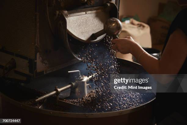 a coffee shop. a person opening a metal shute and coffee beans falling into a roasting drum. - kaffee rösten stock-fotos und bilder