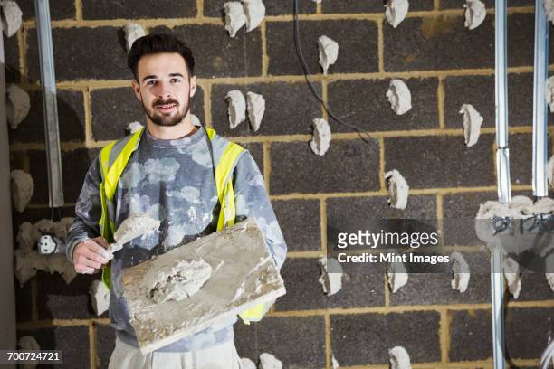 a plasterer, a builder with plasterboard and spreading trowel in front of a cinder block wall. - plasterer stock pictures, royalty-free photos & images
