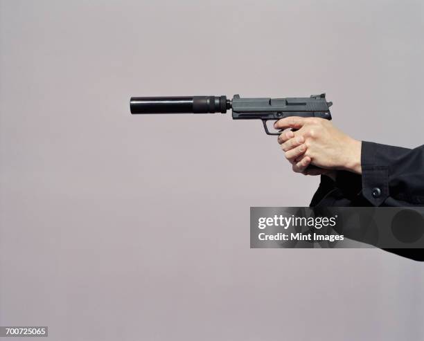 detail of man aiming high powered hand gun with silencer - revolver-with-silencer stock-fotos und bilder
