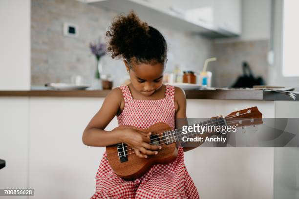 hübsches kind mit karierten kleid spielt ukulele - ukulele stock-fotos und bilder