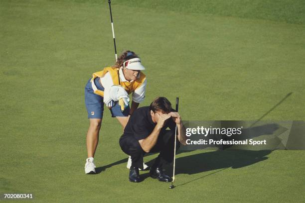 English golfer Nick Faldo pictured crouching down on a green with his caddie Fanny Sunesson to line up a potential shot during play in the 1993 Open...