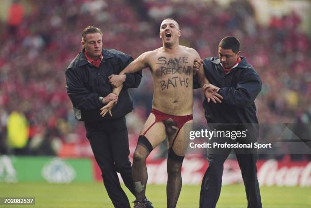 View of a male streaker wearing stockings and suspenders with 'Save Redcar Baths' scrawled on his chest being escorted off the pitch by two stewards...