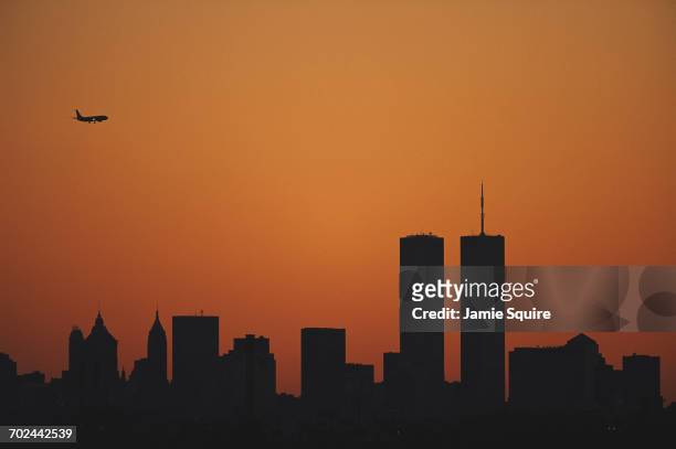 The sun sets at dusk over the Manhattan skyline silhouetting the Twin Towers of the World Trade Center as a passenger jet airliner crosses the sky...