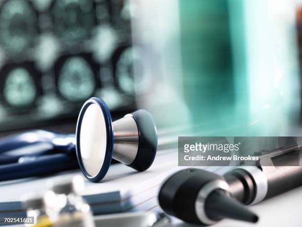 doctors desk with stethoscope sitting on prescription pads, otoscope and mri scan on computer screen - otoscope foto e immagini stock