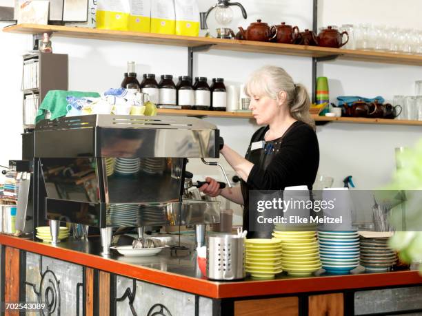 mature waitress making coffee using coffee machine behind counter - melbourne cafe stock-fotos und bilder