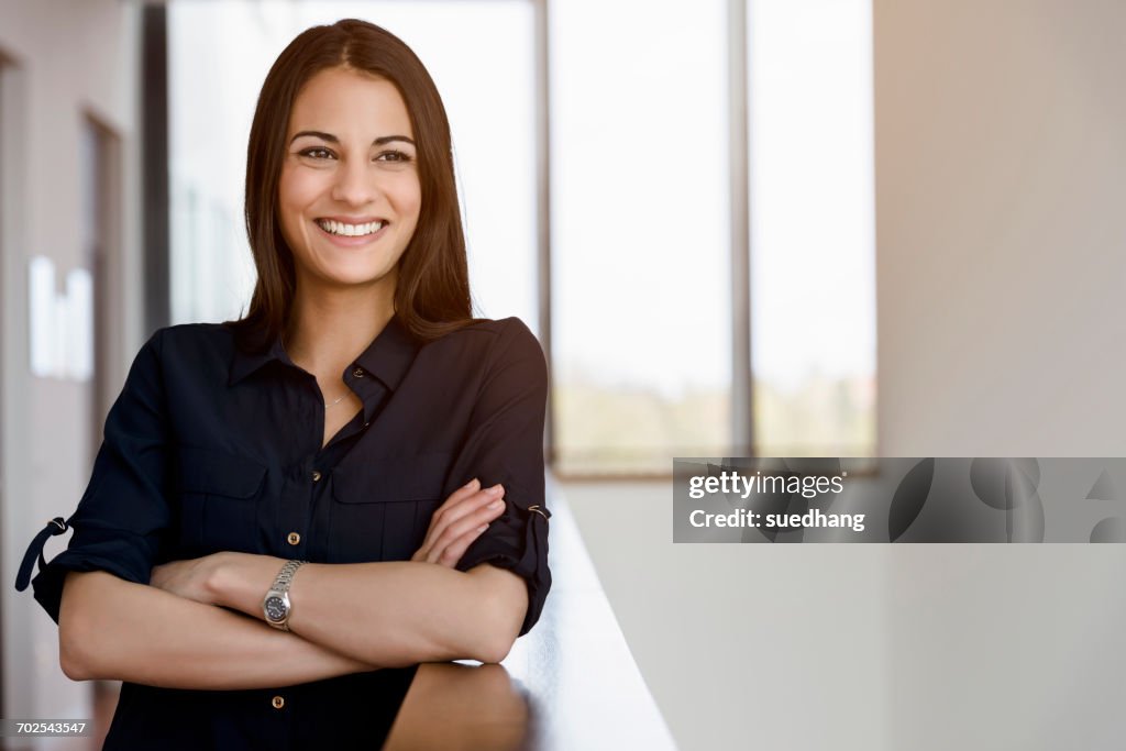 Young businesswoman with arms folded in office corridor