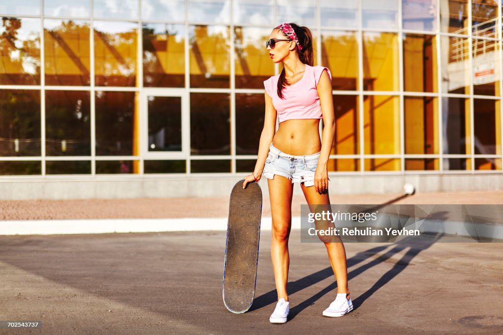 Portrait of young woman standing outdoors, holding skateboard