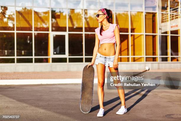 portrait of young woman standing outdoors, holding skateboard - oberteil stock-fotos und bilder