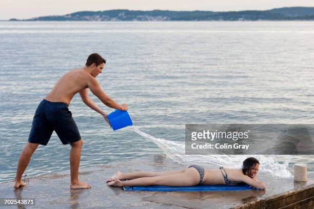 young man throwing bucket of water over female sunbather, orebic, croatia - throwing water stock pictures, royalty-free photos & images