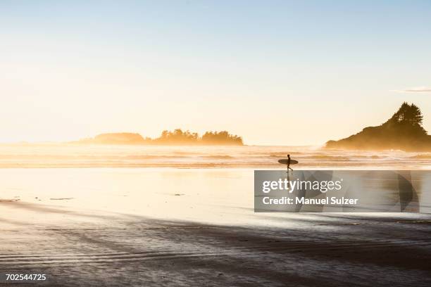 male surfer carrying surfboard on long beach, pacific rim national park, vancouver island, british columbia, canada - long beach britisch kolumbien stock-fotos und bilder