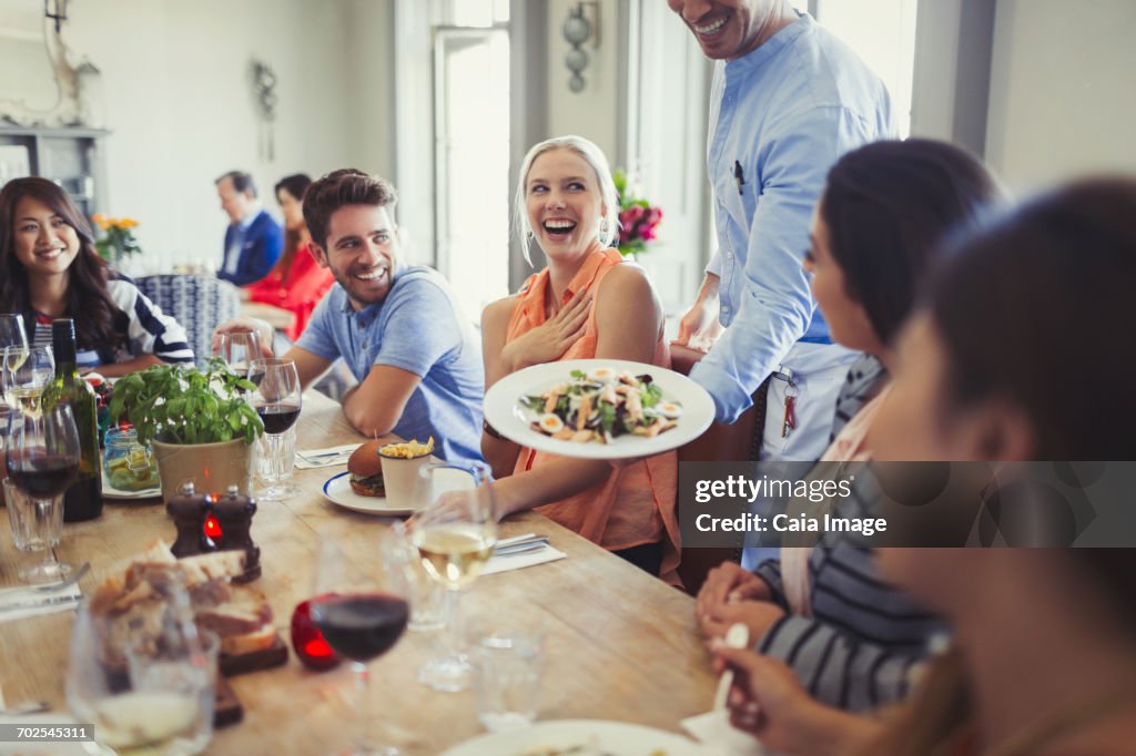 Waiter serving salad to woman dining with friends at restaurant table