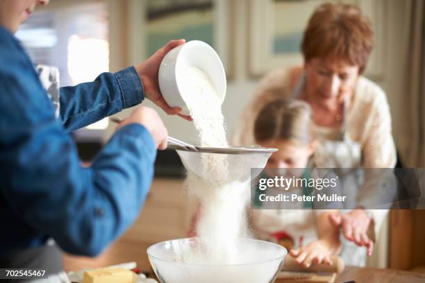senior woman and granddaughters sifting flour for cookies - flour sifter stock pictures, royalty-free photos & images