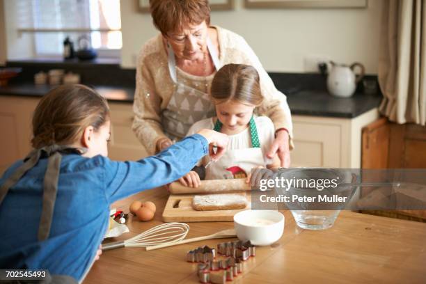 senior woman and granddaughters rolling dough for christmas tree cookies - rolling pin stock pictures, royalty-free photos & images