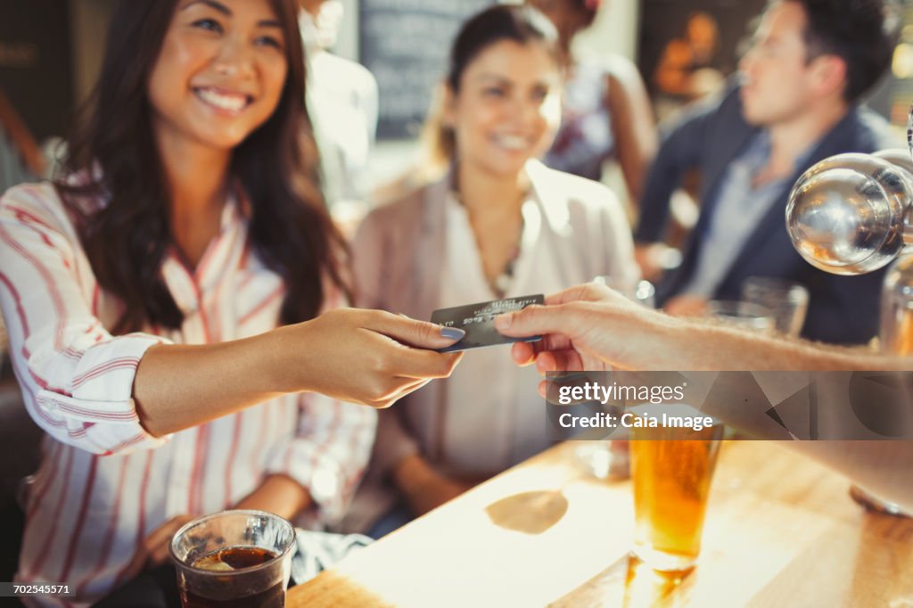 Smiling woman paying bartender with credit card at bar