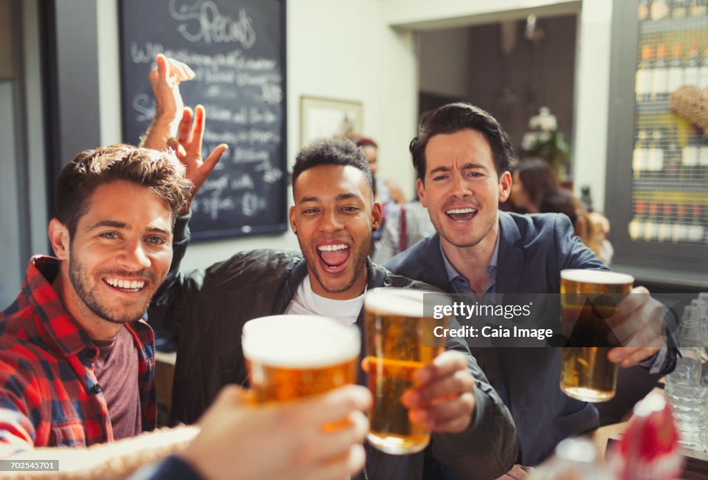 Portrait enthusiastic men friends toasting beer glasses at bar