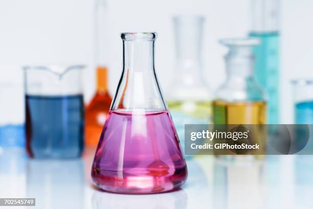 erlenmeyer flask containing a solution of potassium permanganate (kmno4), various flasks with transition metal salts, dry chemicals and solutions in background - labor chemie stock-fotos und bilder
