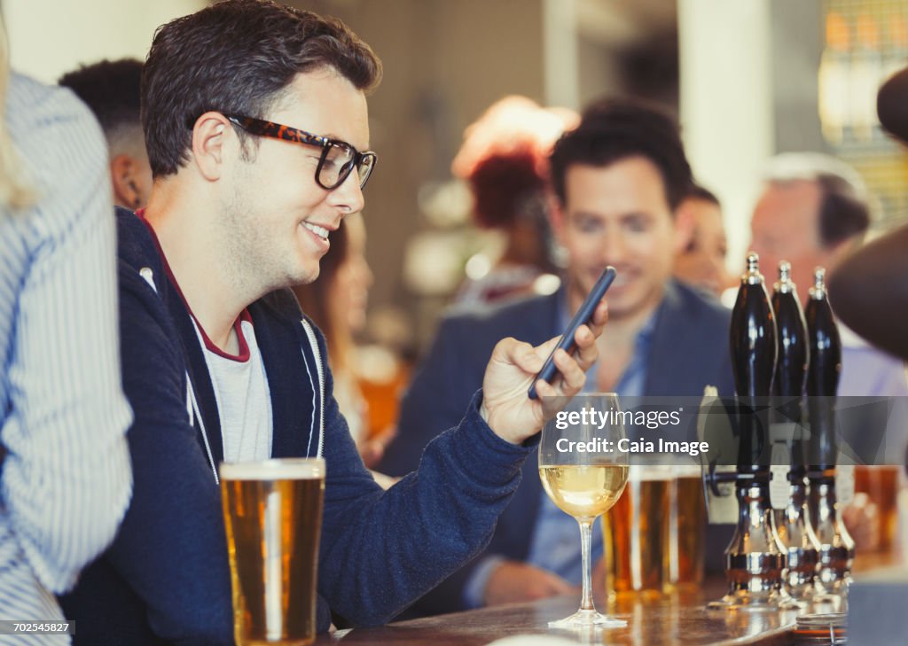 Smiling man texting with cell phone drinking wine at bar