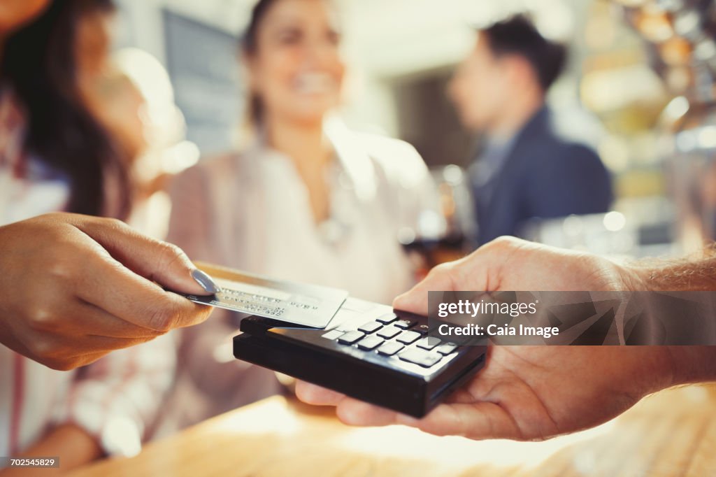 Woman with credit card paying bartender with contactless payment at bar