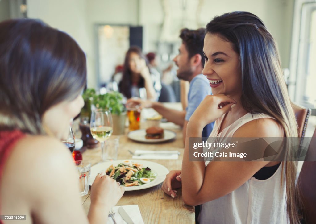 Smiling women friends talking and eating at restaurant table