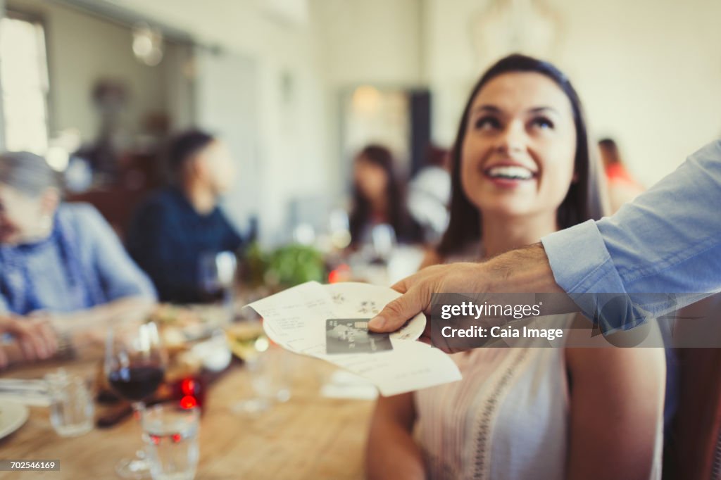 Waiter returning bill and credit card to woman dining at restaurant table