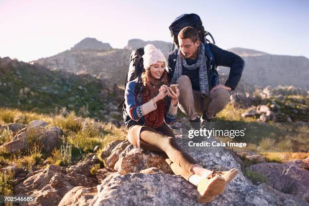 young couple with backpacks hiking, resting on rock using smart phone - two women on phone isolated stock pictures, royalty-free photos & images