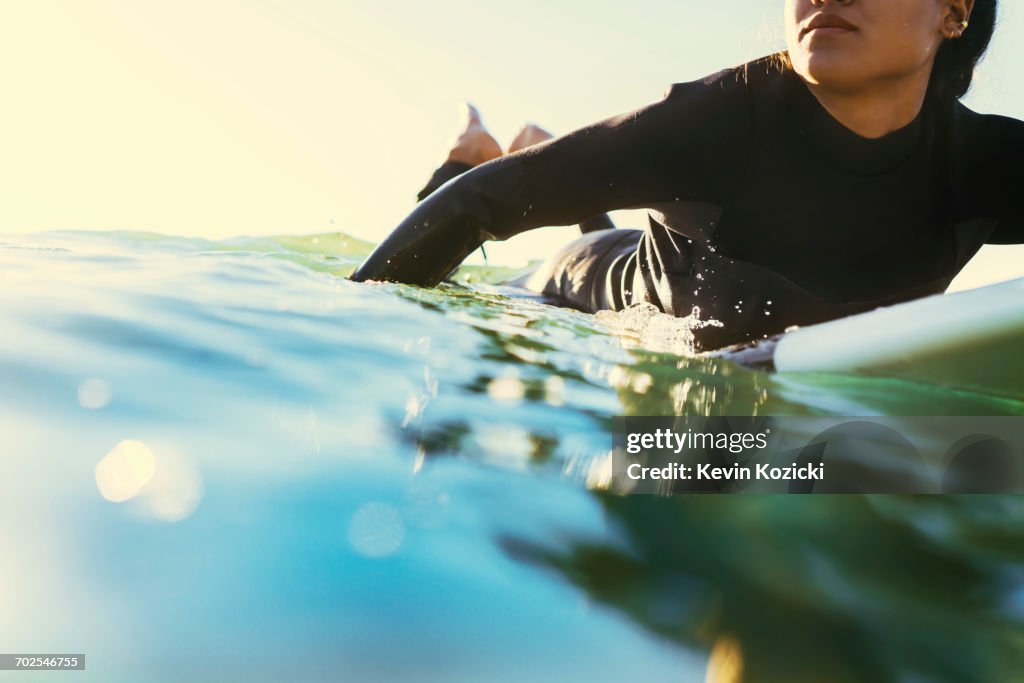 Young female surfer paddling surfboard at sea, Newport Beach, California, USA