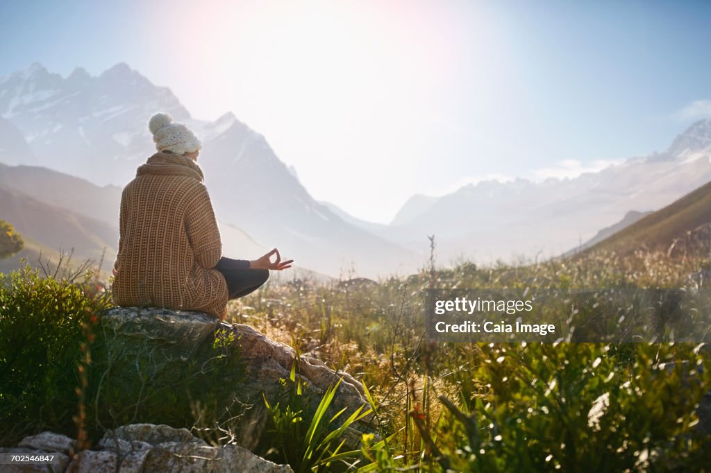 Young woman meditating on rock in sunny, remote valley
