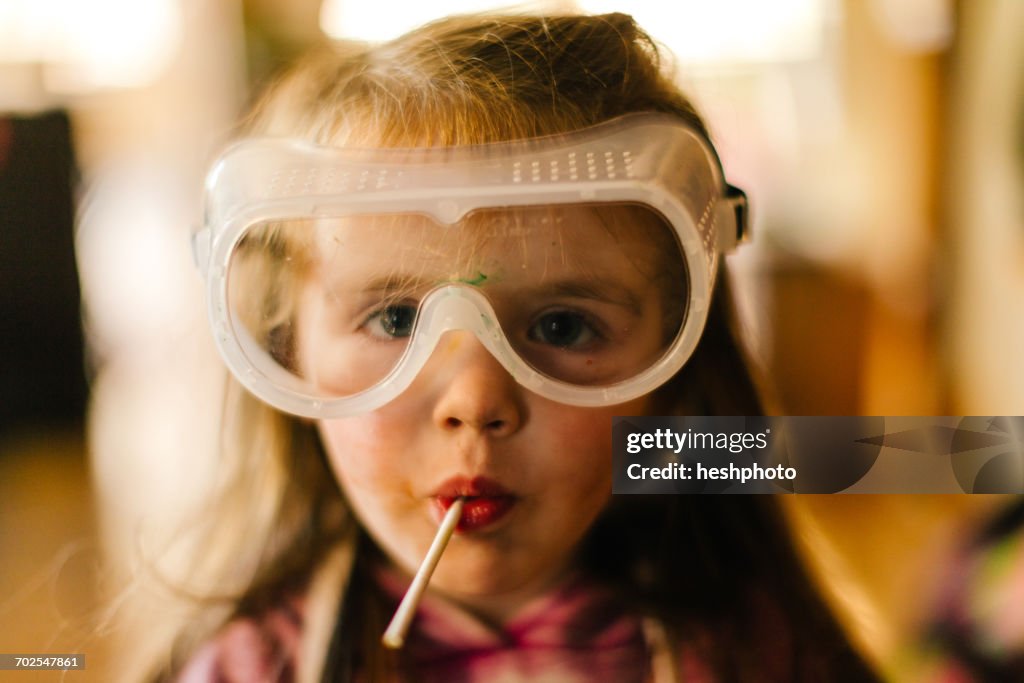 Portrait of girl in safety goggles sucking lollipop