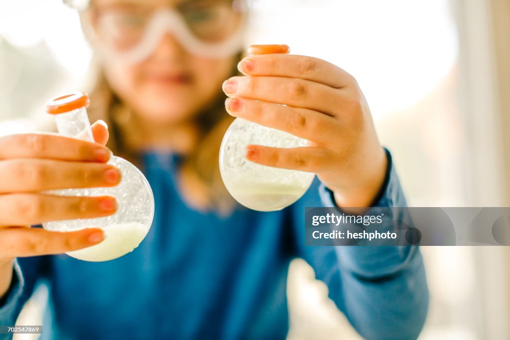 Girl doing science experiment, holding flasks of liquid