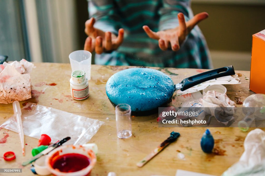 Hands of girl doing science experiment, blue liquid foaming in frying pan