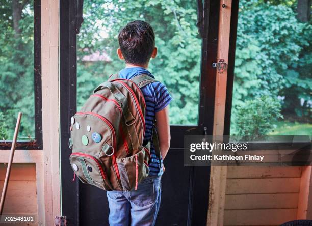 rear view of schoolboy looking through porch window - satchel bag stock-fotos und bilder