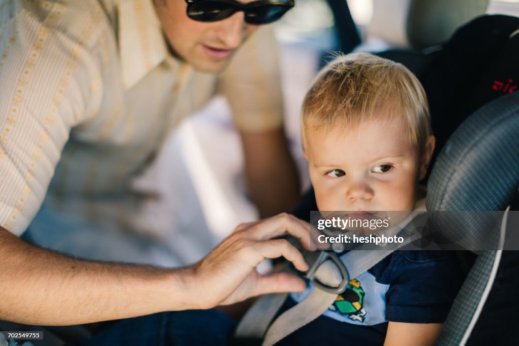 Father securing young son in car seat