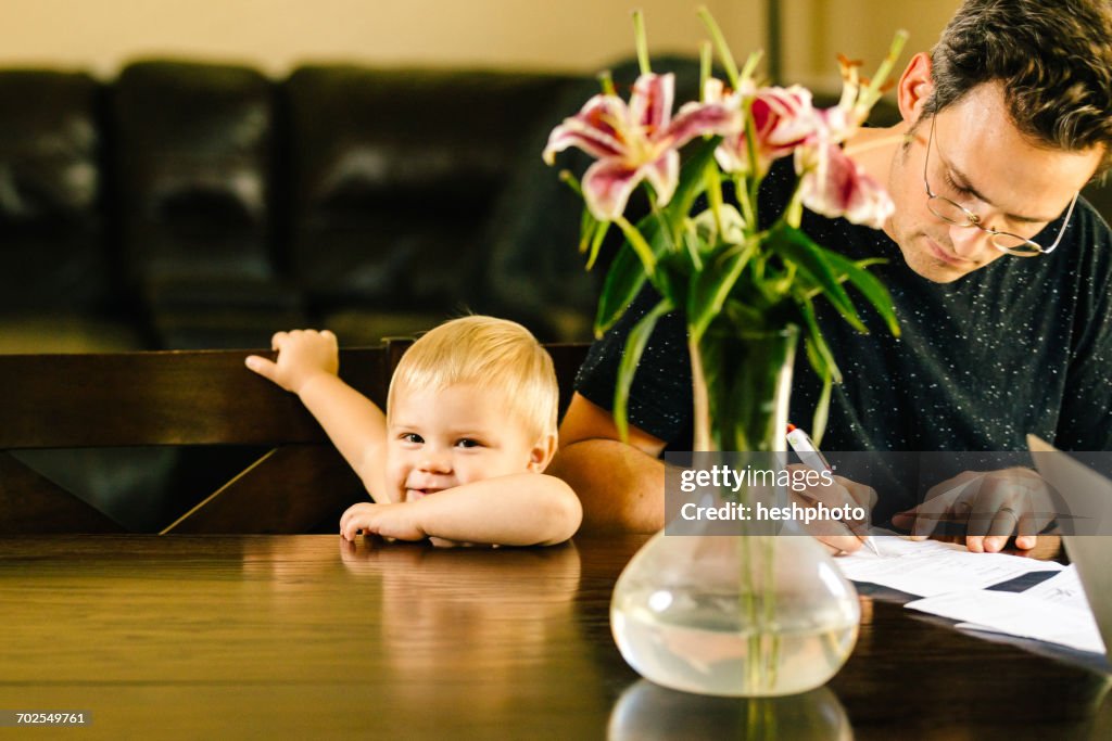 Father and young son sitting at table, father writing on document