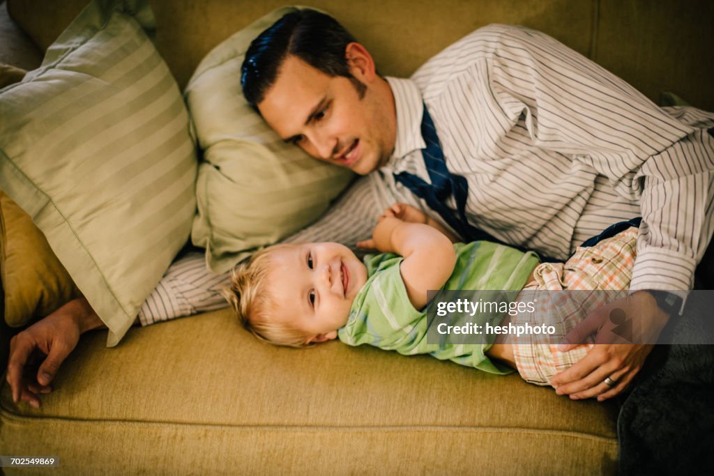 Father and young son lying on sofa together