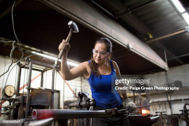 female metalsmith hammering red hot metal rod on workshop anvil - schmied stock-fotos und bilder