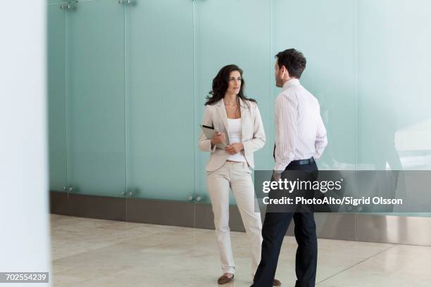 businesswoman chatting with male colleague in office corridor - mid distance stock pictures, royalty-free photos & images