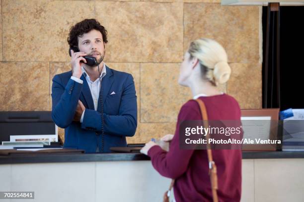 impatient customer waiting while hotel receptionist talks on phone - ignoring fotografías e imágenes de stock