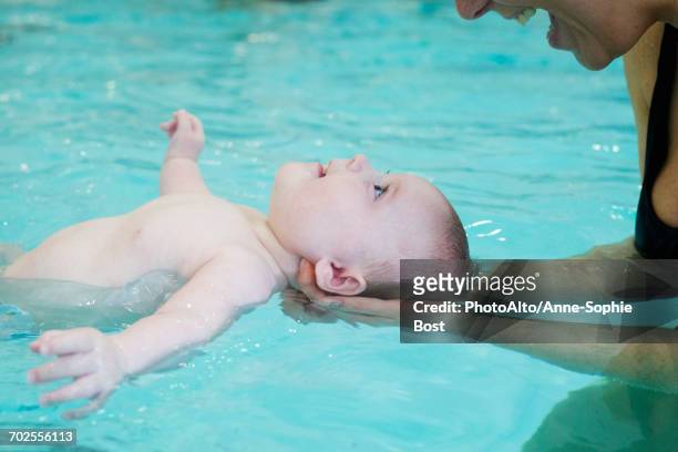 mother teaching infant how to float in swimming pool - babyschwimmen stock-fotos und bilder