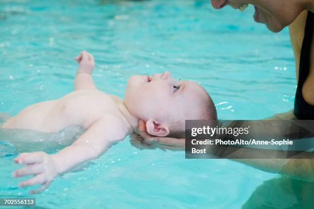 mother teaching infant how to float in swimming pool - baby bath stock pictures, royalty-free photos & images