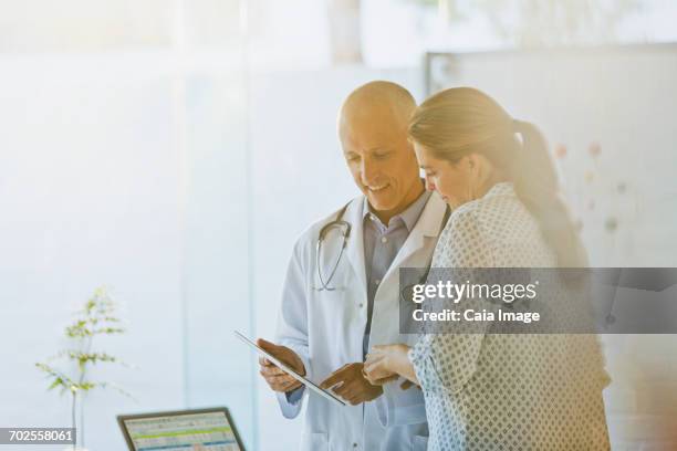 male doctor showing digital tablet to female patient in doctors office - flouté photos et images de collection