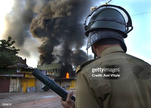 An Indian state police officer watches a Muslim owned shop burn March 1, 2002 in Ahmadabad, India, two days after a Muslim mob attacked a train,...